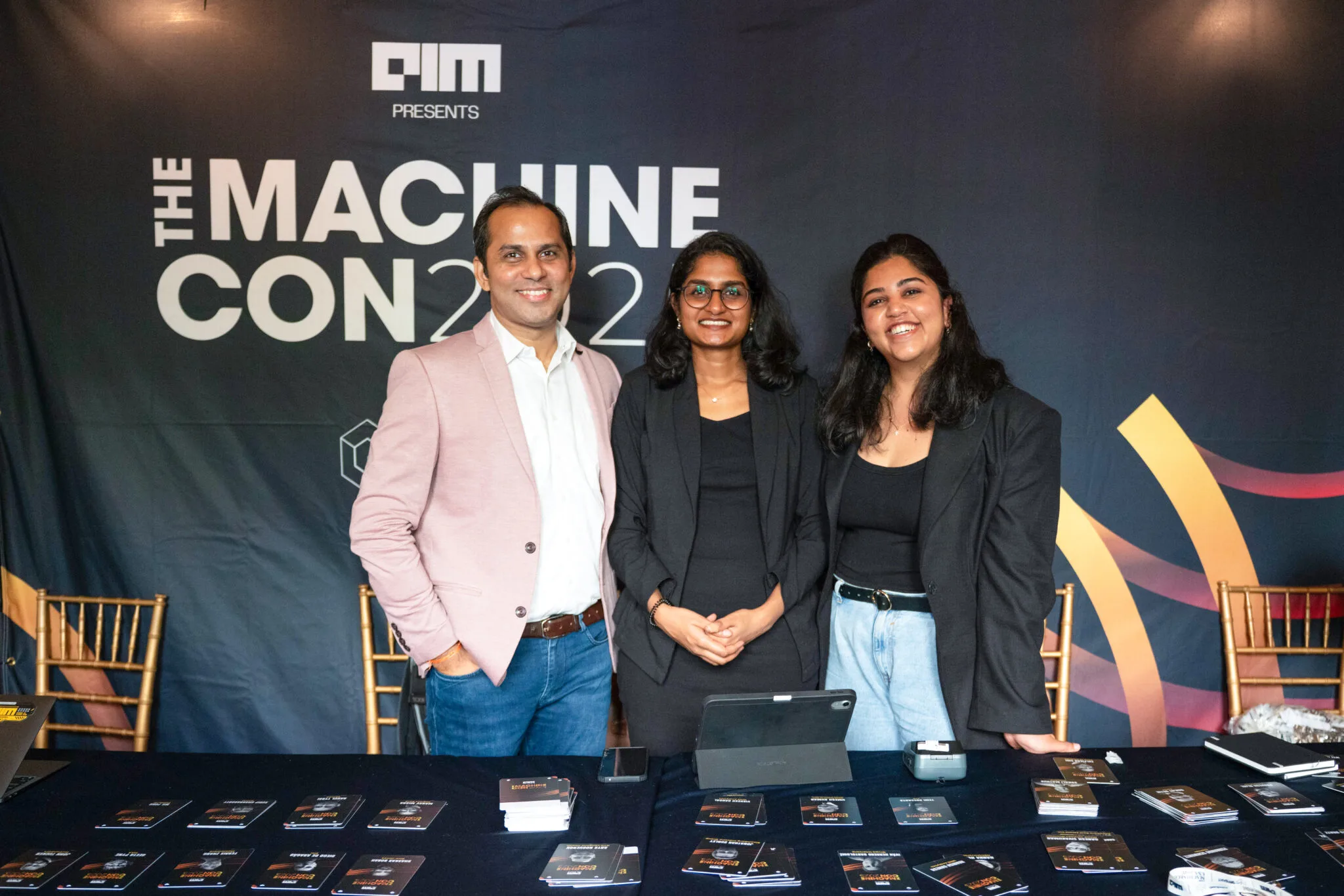 Three people smiling at booth at MachineCon New York 2025